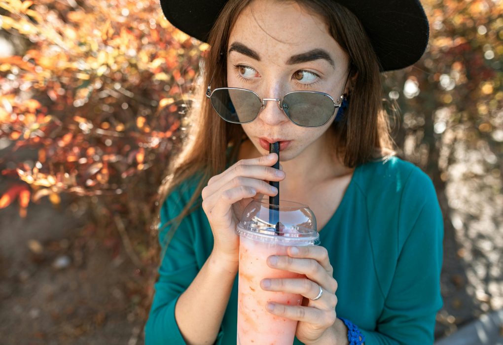 Why Does My Tooth Hurt When I Drink Something Cold? Find Out If It’s a Cavity, Crack, or Something Worse woman wearing sunglasses sipping a smoothie through a straw