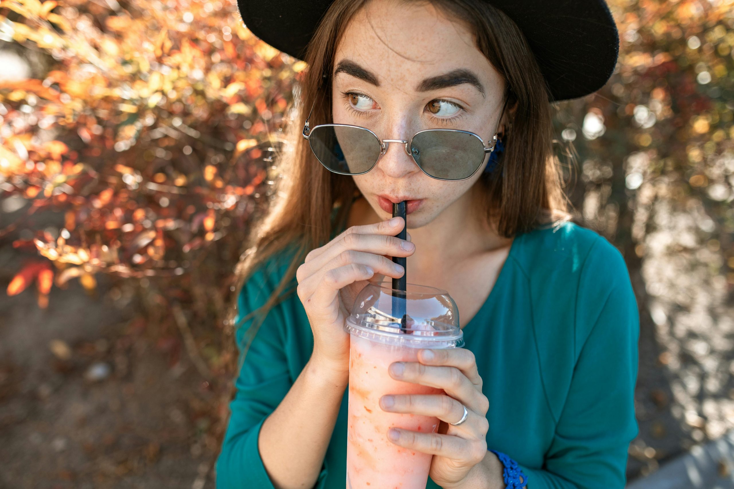 woman wearing sunglasses sipping a smoothie through a straw