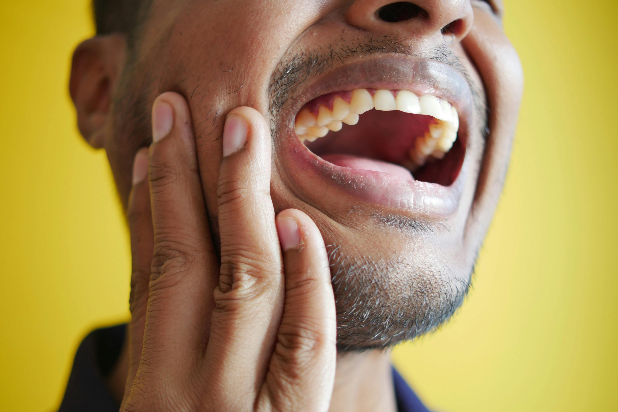 man in pain with his mouth open, one hand pressing against his jaw